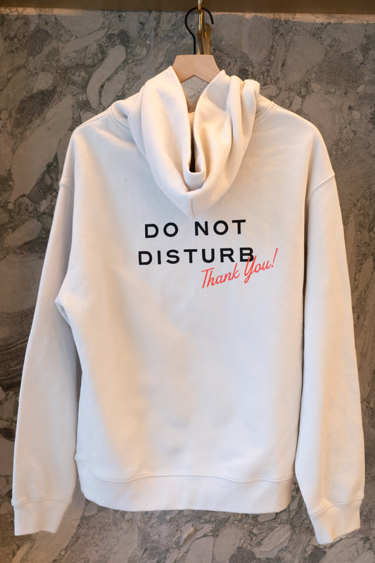 White hoodie with 'DO NOT DISTURB Thank You!' text on a hanger against a marble wall.