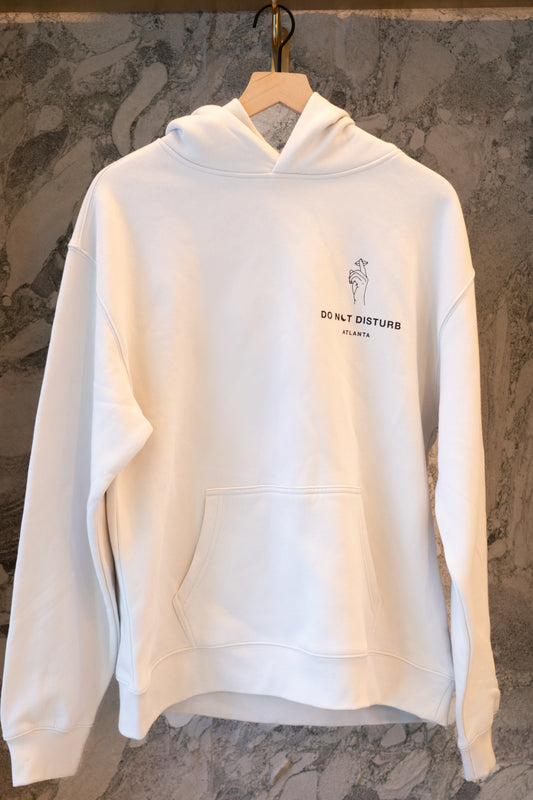 Do not disturb ATL White hoodie with text on a hanger against a marble wall